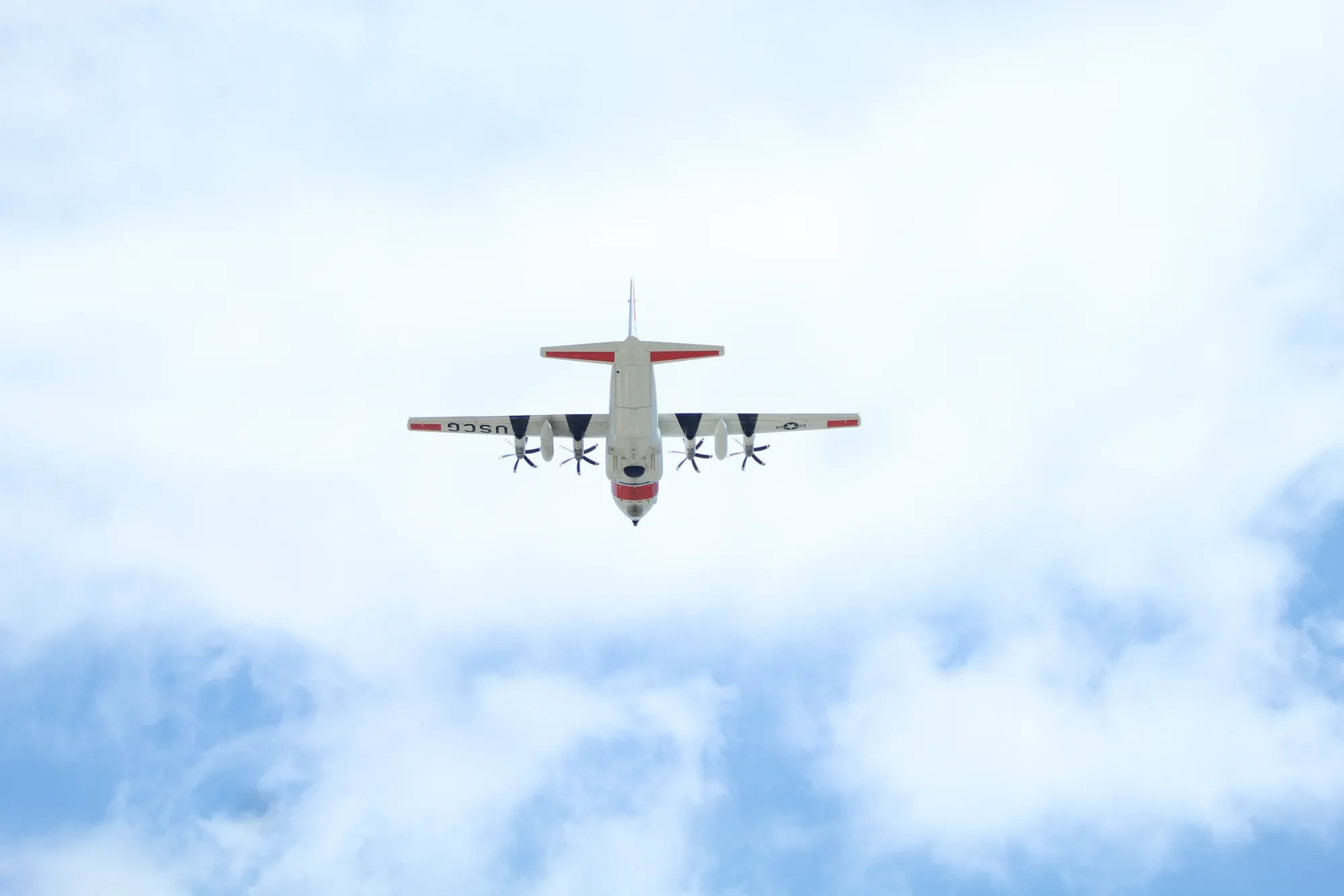 U.S. Coast Guard aircraft flying overhead against a clouded sky