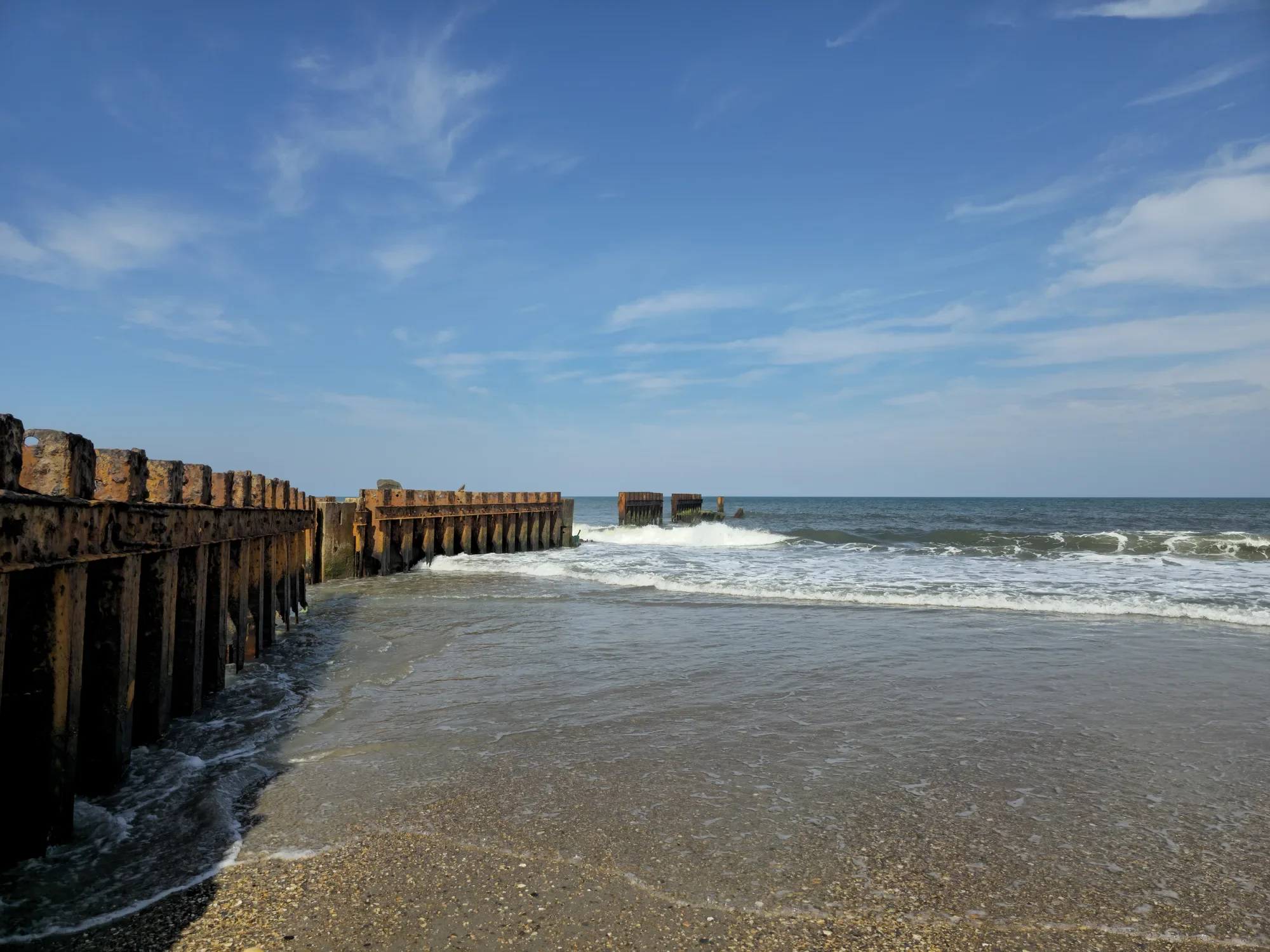 Waves breaking beside weathered timber groynes on a sunny beach