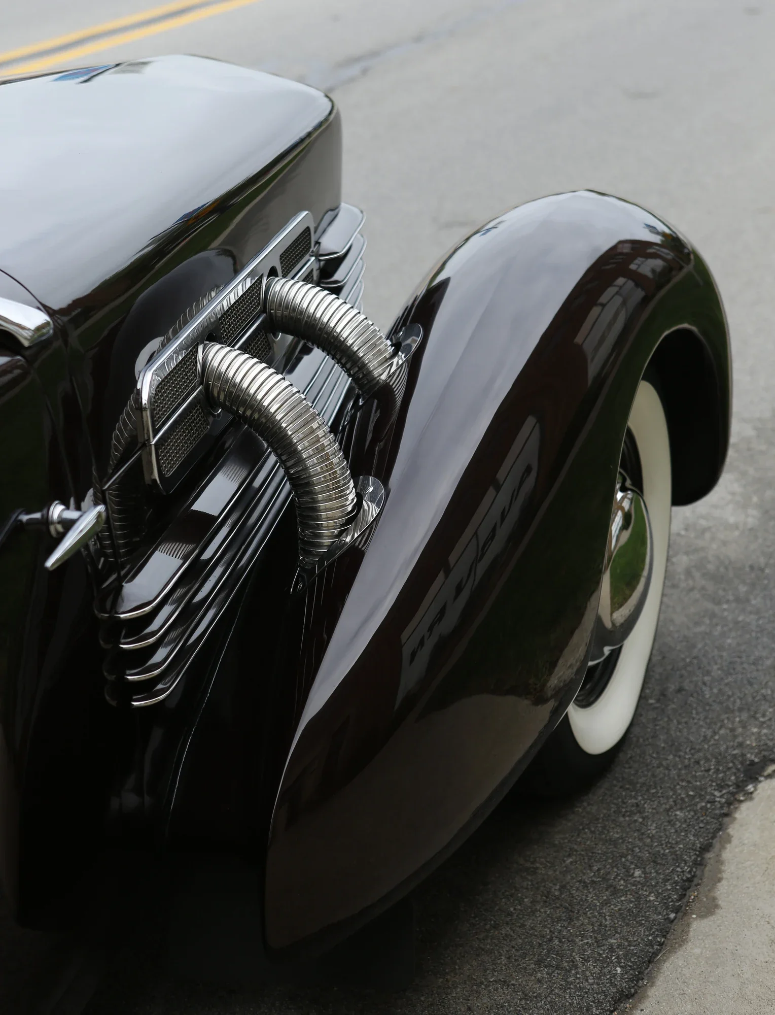 Black vintage automobile fender, whitewall tire, and curved external pipes