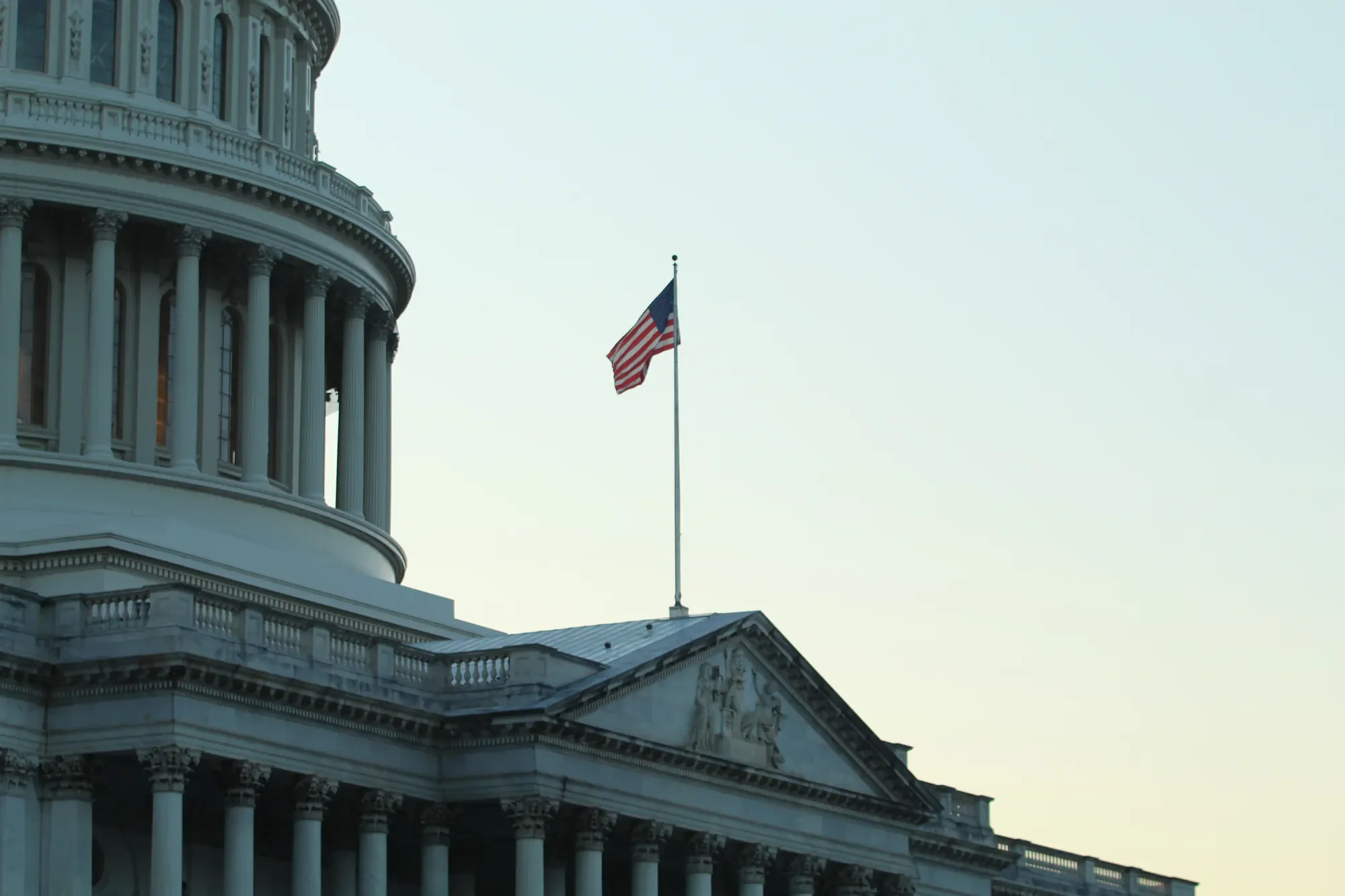United States Capitol columns and flag at dusk