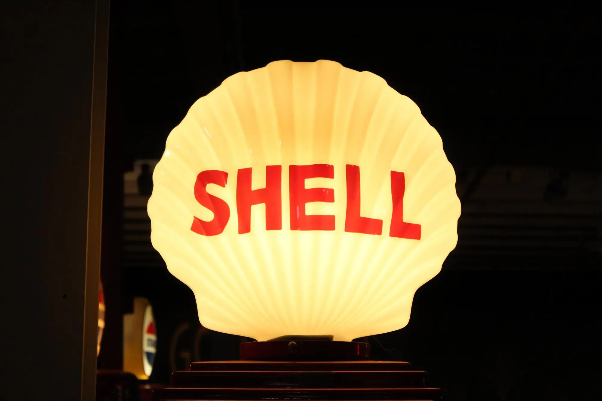 Illuminated Shell gasoline sign against a dark museum interior