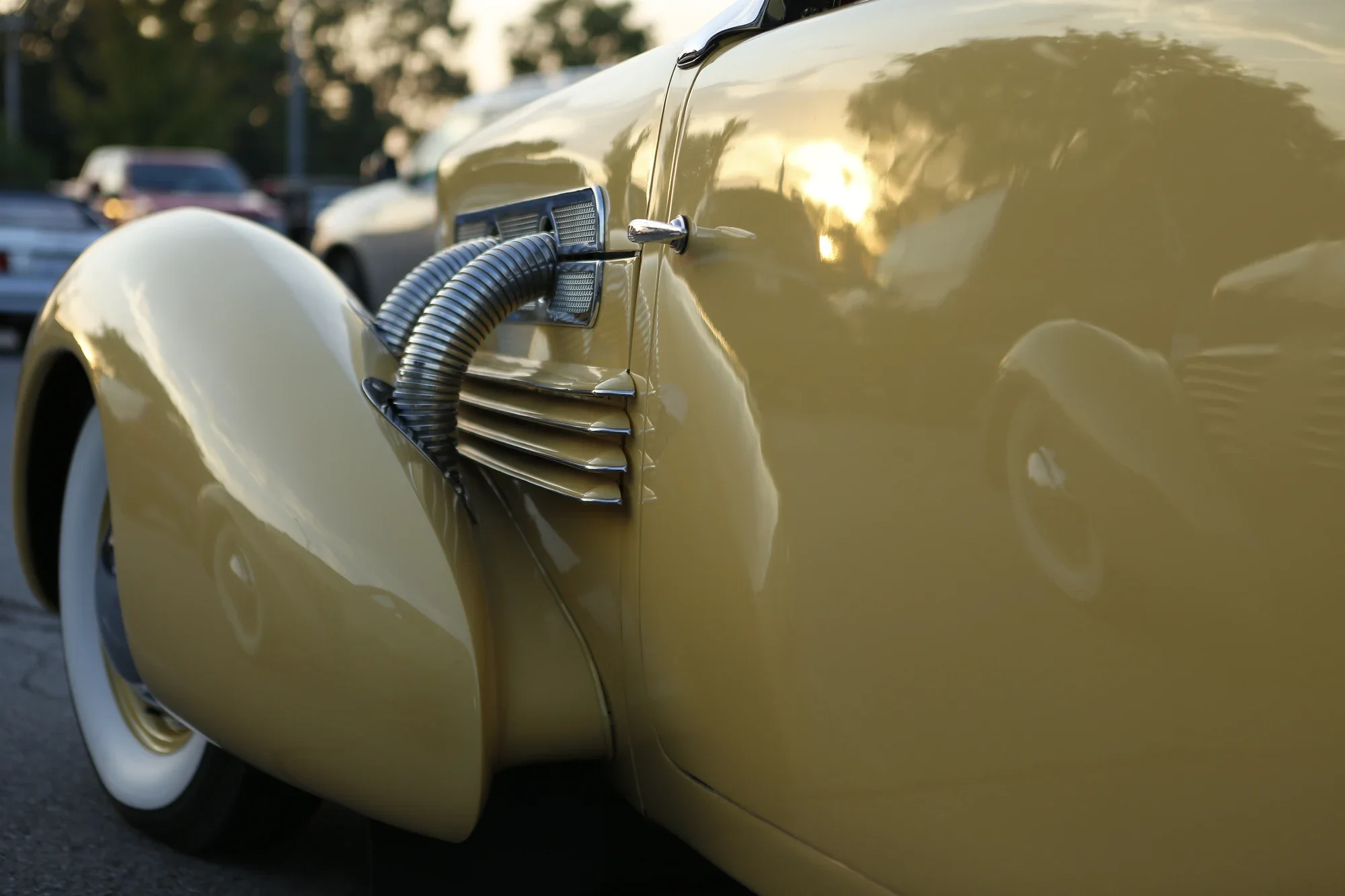 Curved cream automobile bodywork and external pipes reflecting warm evening light