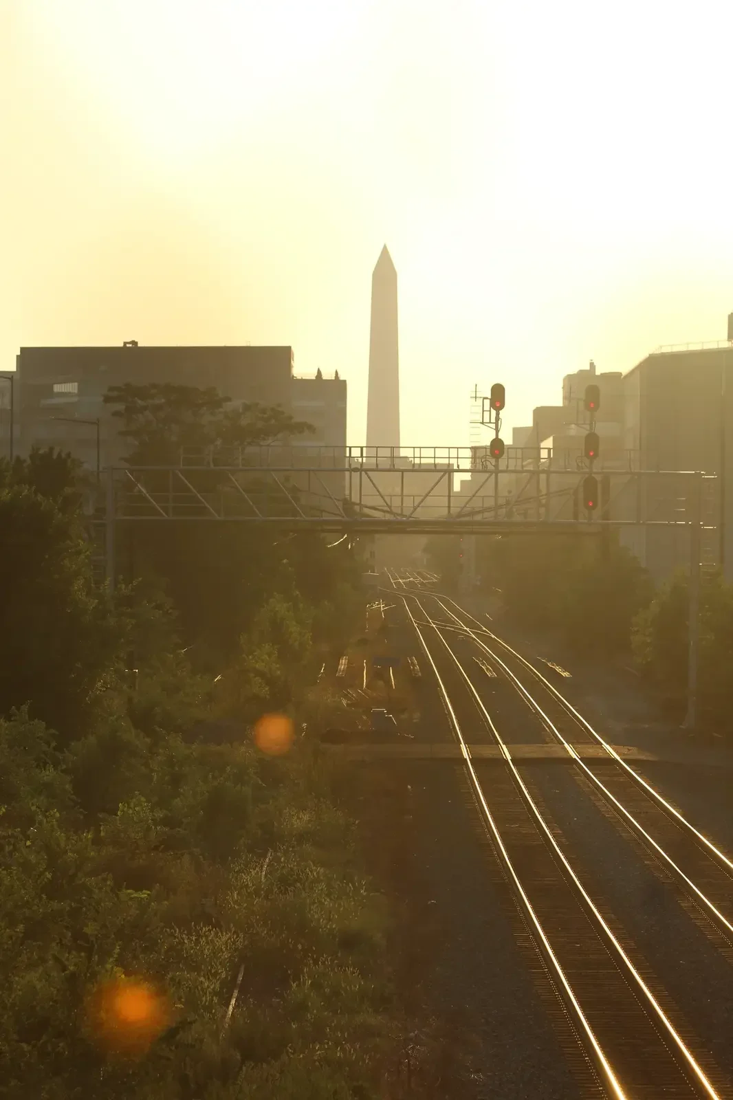 Washington Monument rising beyond rail lines in warm evening light