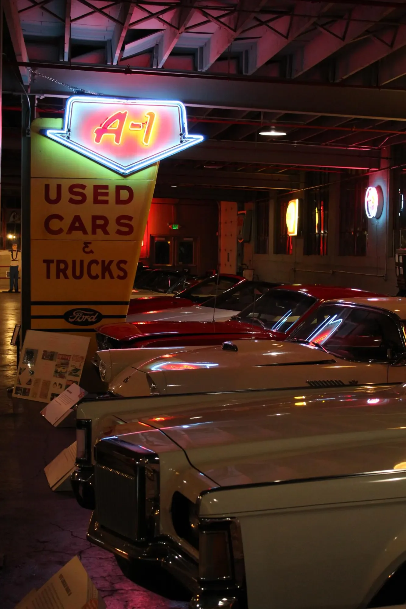 Classic automobiles beneath neon dealership signs