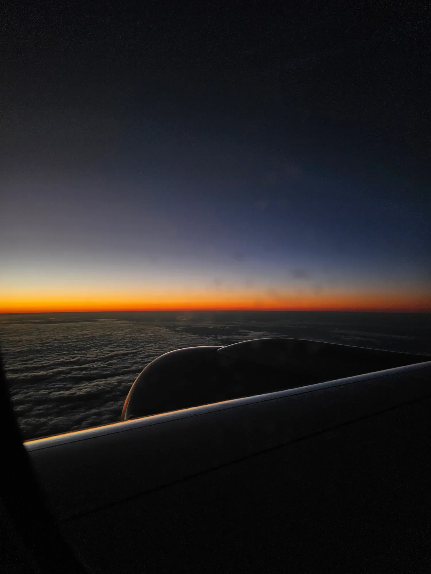 Aircraft wing silhouetted against a narrow sunset horizon