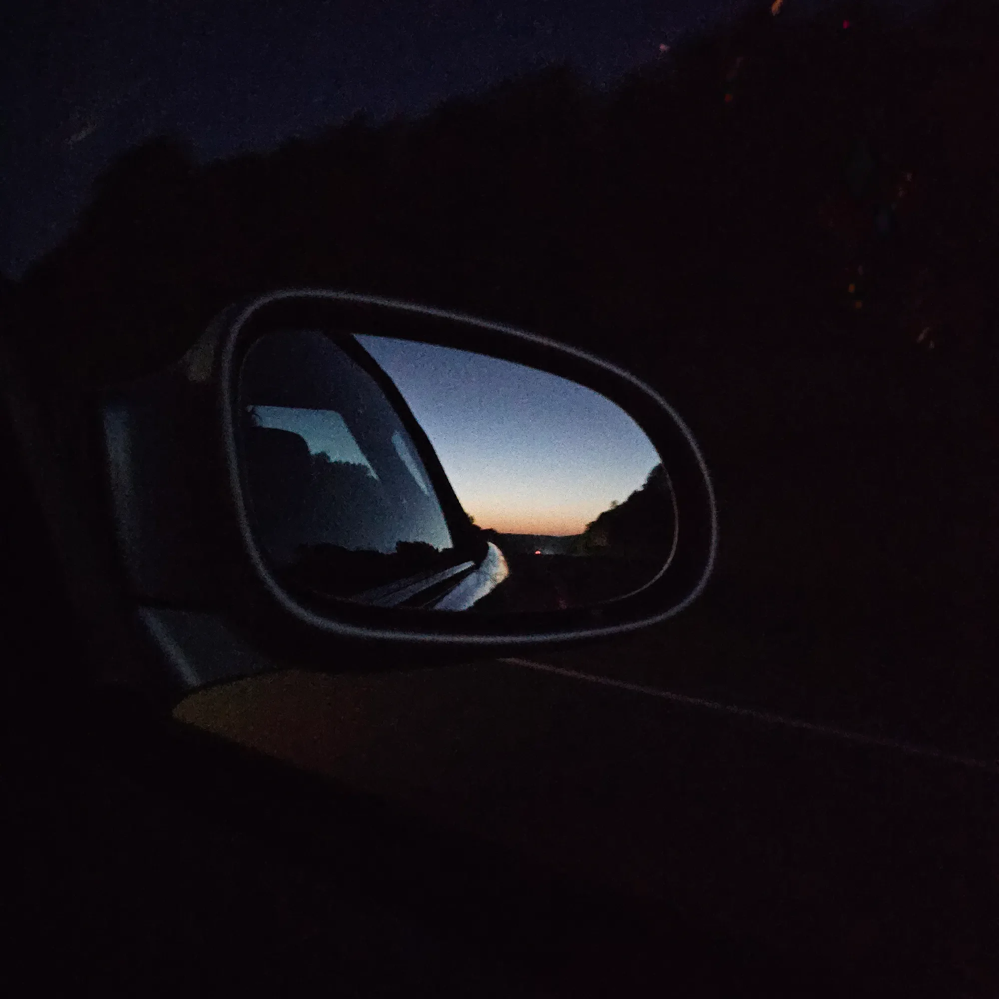 Last light reflected in a car mirror during a night drive