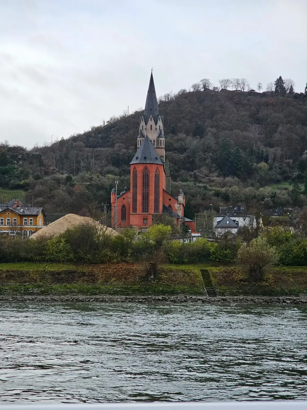 Red riverside church beneath a wooded hillside