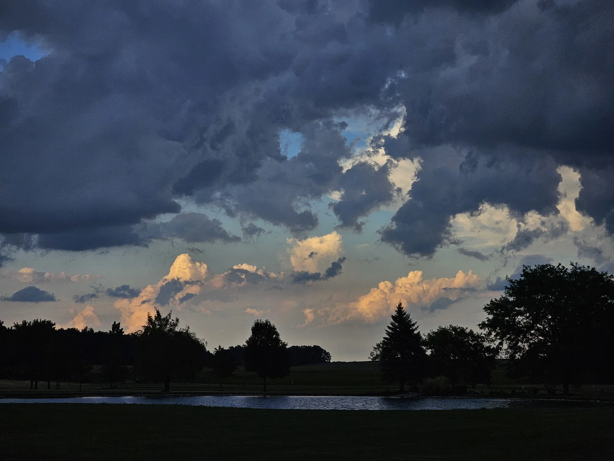 Dark storm clouds gathering above water and a tree-lined shore