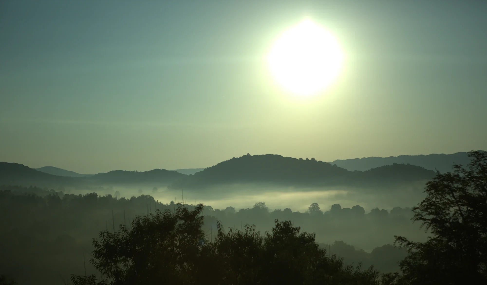 Bright morning sun above layers of fog-covered hills