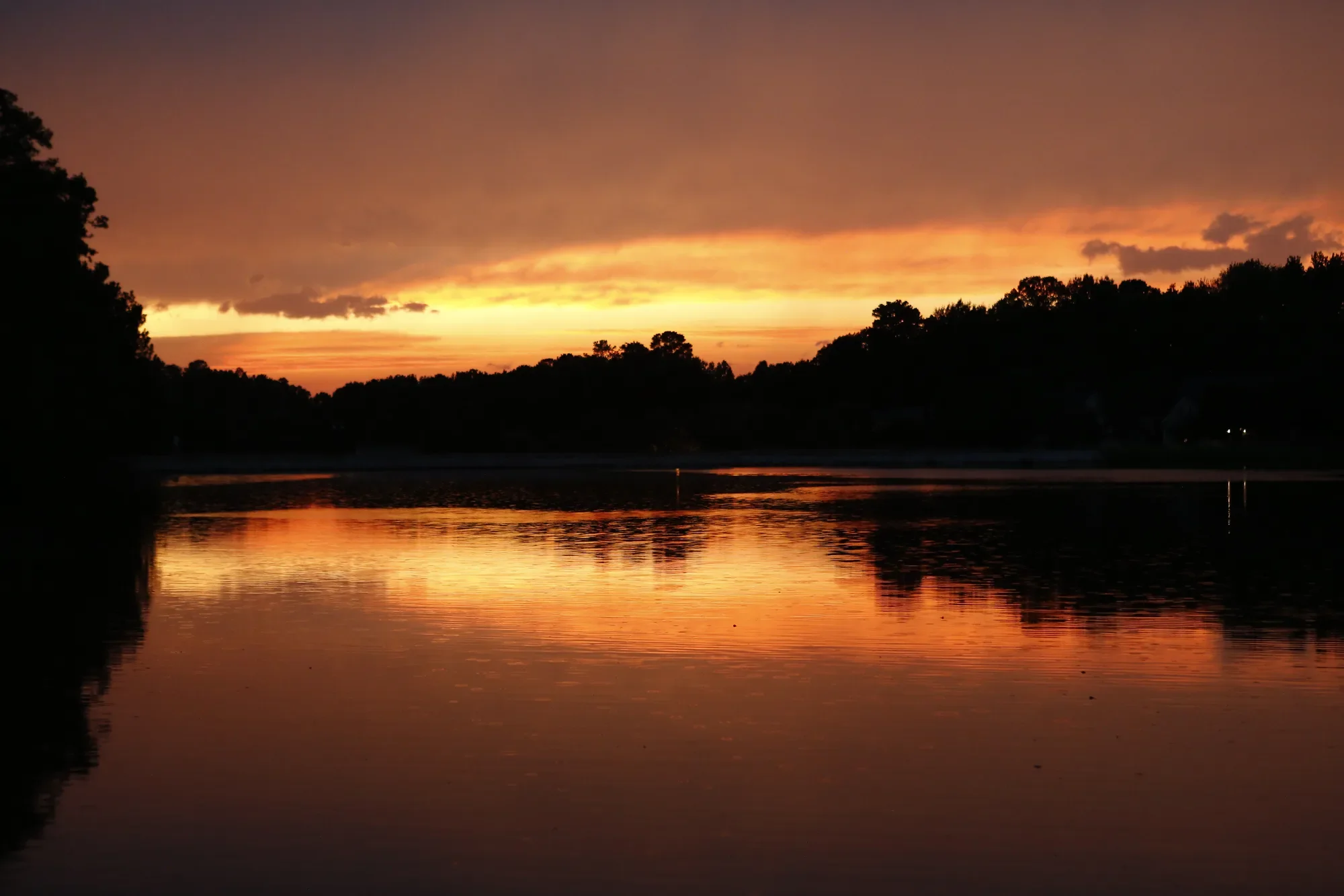 Orange sunset reflected across a lake beneath dark clouds