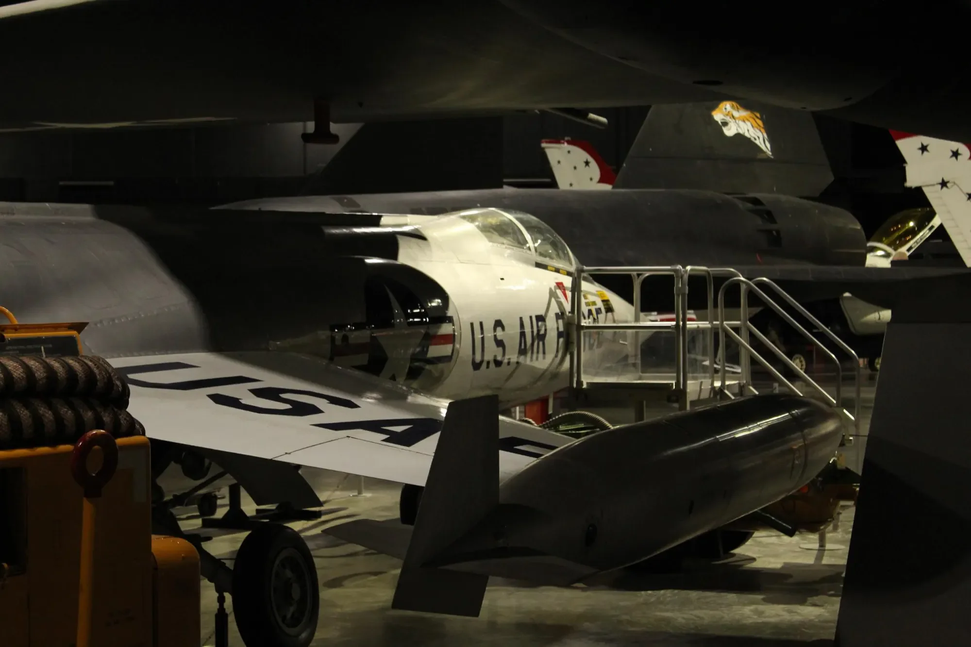 Silver U.S. Air Force jet displayed among other aircraft in a dark museum gallery